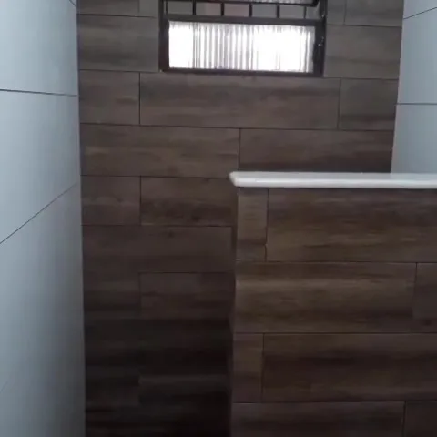 Banheiro reformado, com revestimento que imita madeira na parede do fundo